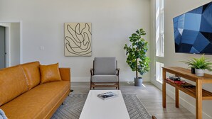 Un soggiorno con un divano in pelle, una poltrona grigia, un tavolino da caffè, un quadro astratto di grandi dimensioni, una pianta in vaso e un televisore su un supporto in legno.