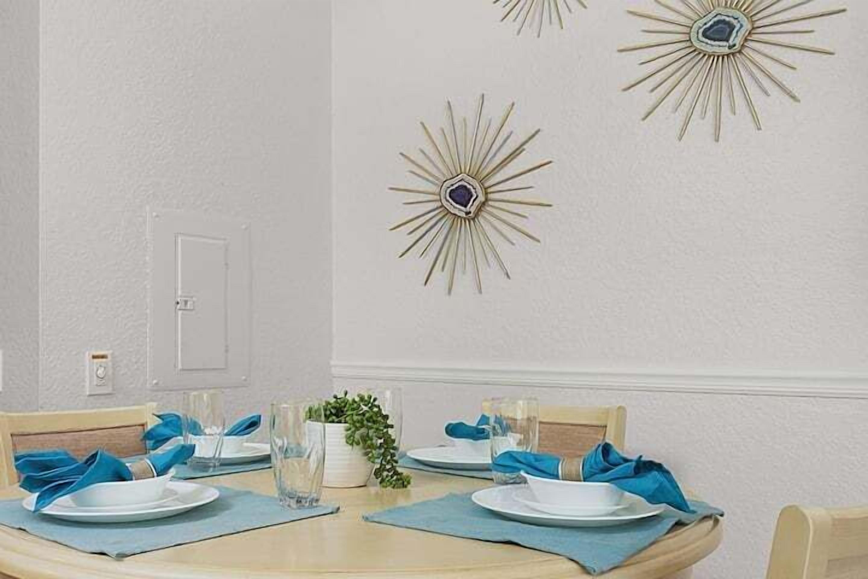 Een eetruimte met een ronde tafel voor vier personen, blauwe placemats en decoratieve wandkunst.