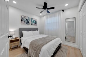 Ein Schlafzimmer mit Bett, Nachttisch, Deckenventilator, Spiegel und Bildern an der Wand.