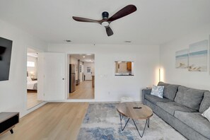 Ein modernes Wohnzimmer mit einem grauen Sofa, einem runden Couchtisch und einem Deckenventilator.