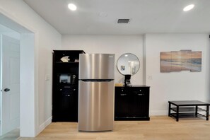 Une cuisine moderne avec un réfrigérateur en acier inoxydable, un meuble noir, un miroir rond et un tableau représentant une scène de plage accroché au mur.
