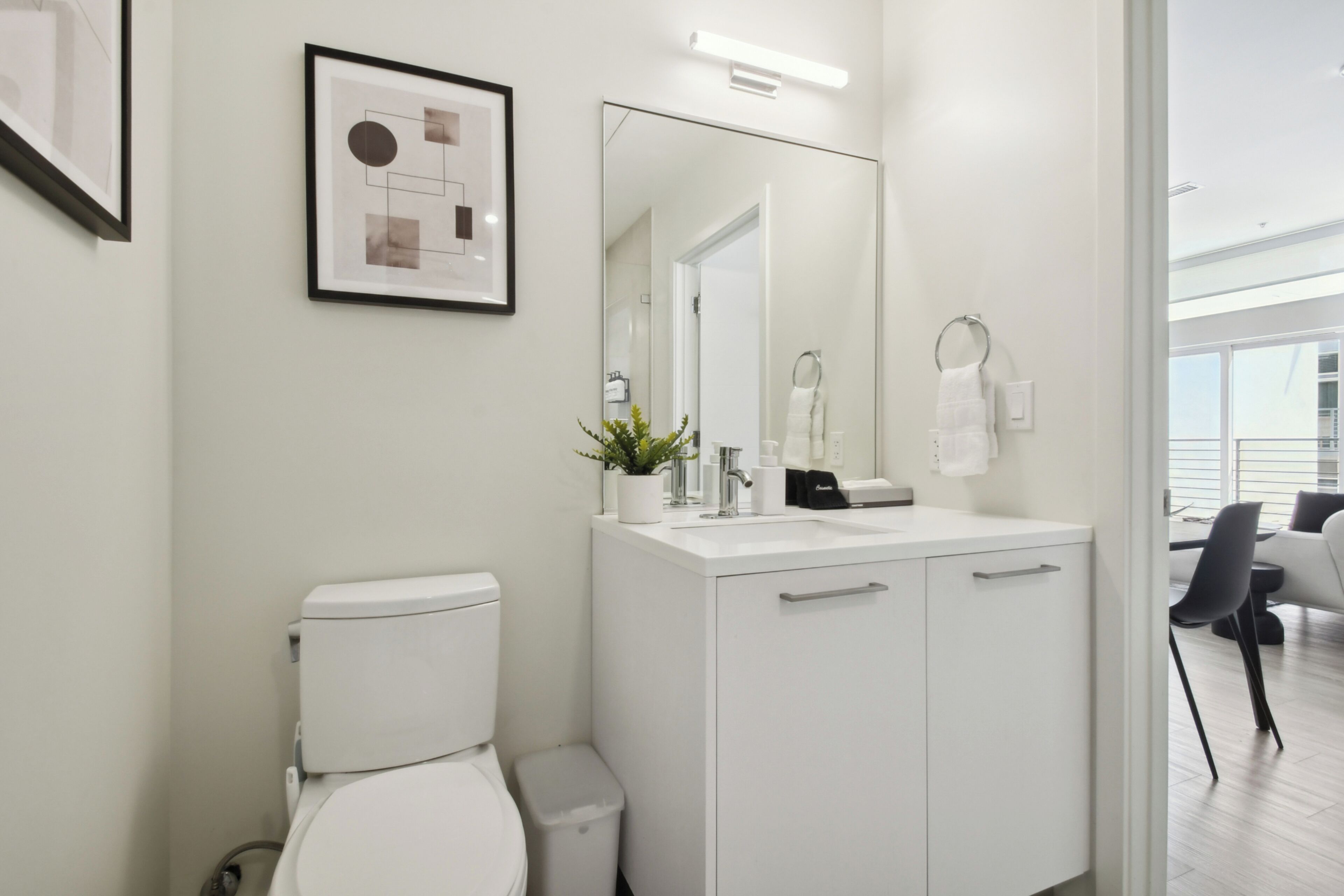 A modern bathroom with a white toilet, a sink with a mirror, and a framed picture on the wall.