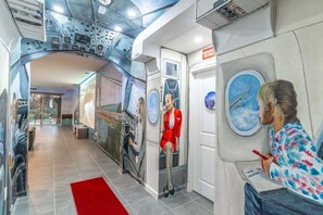Un couloir avec une moquette rouge, une fresque murale et une personne en train de peindre.