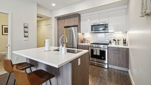 Une cuisine moderne dotée d’un îlot central, d’appareils électroménagers en acier inoxydable et de meubles de rangement en bois.