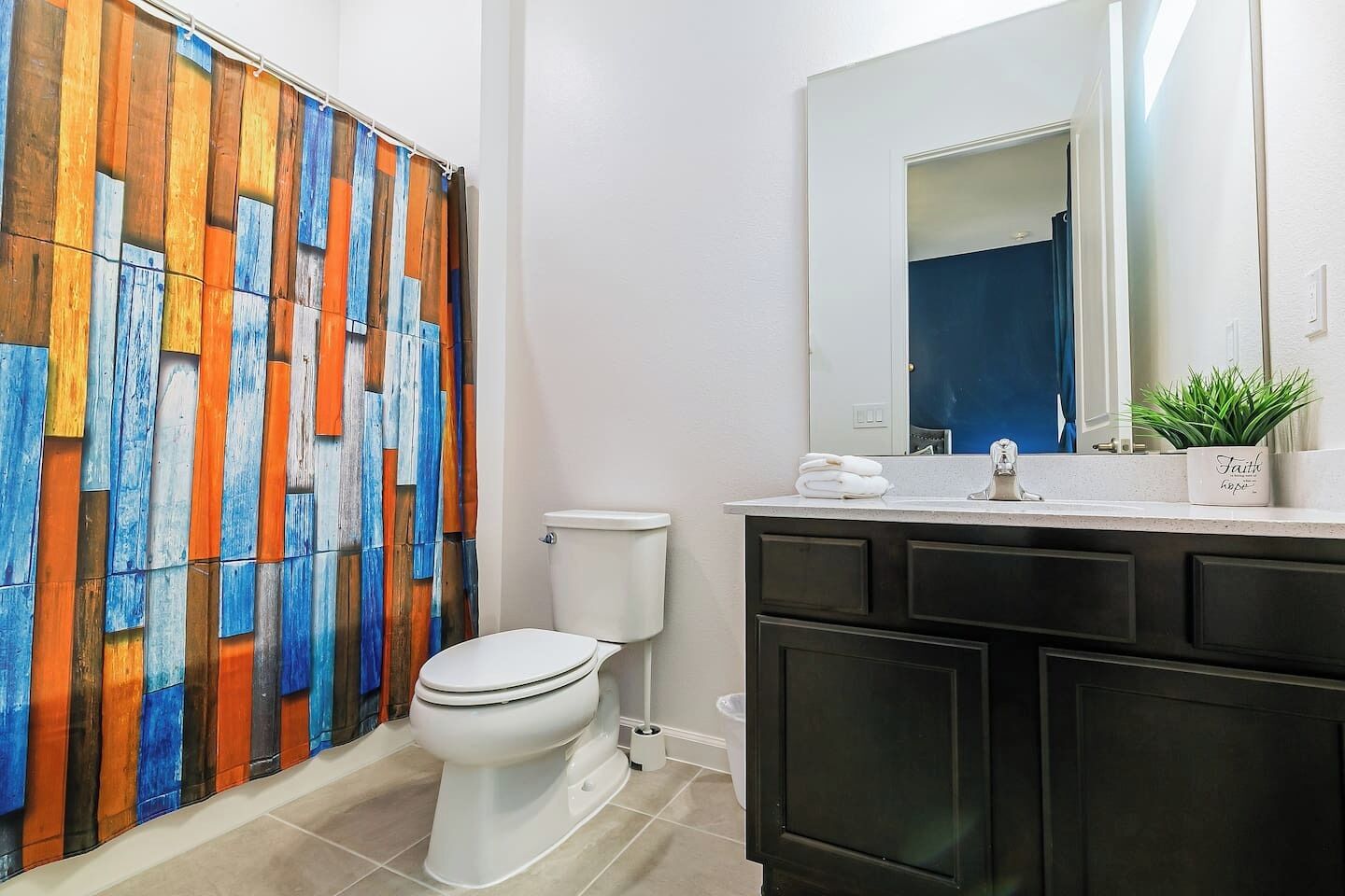 Une salle de bain au design moderne, avec des toilettes blanches, un meuble-lavabo foncé et un rideau de douche en bois aux couleurs vives.