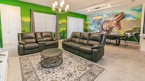 A living room with two leather sofas, a coffee table, and a mural of a dinosaur on the wall. - 2476 Shanti Drive 12bed (Kissimmee)
