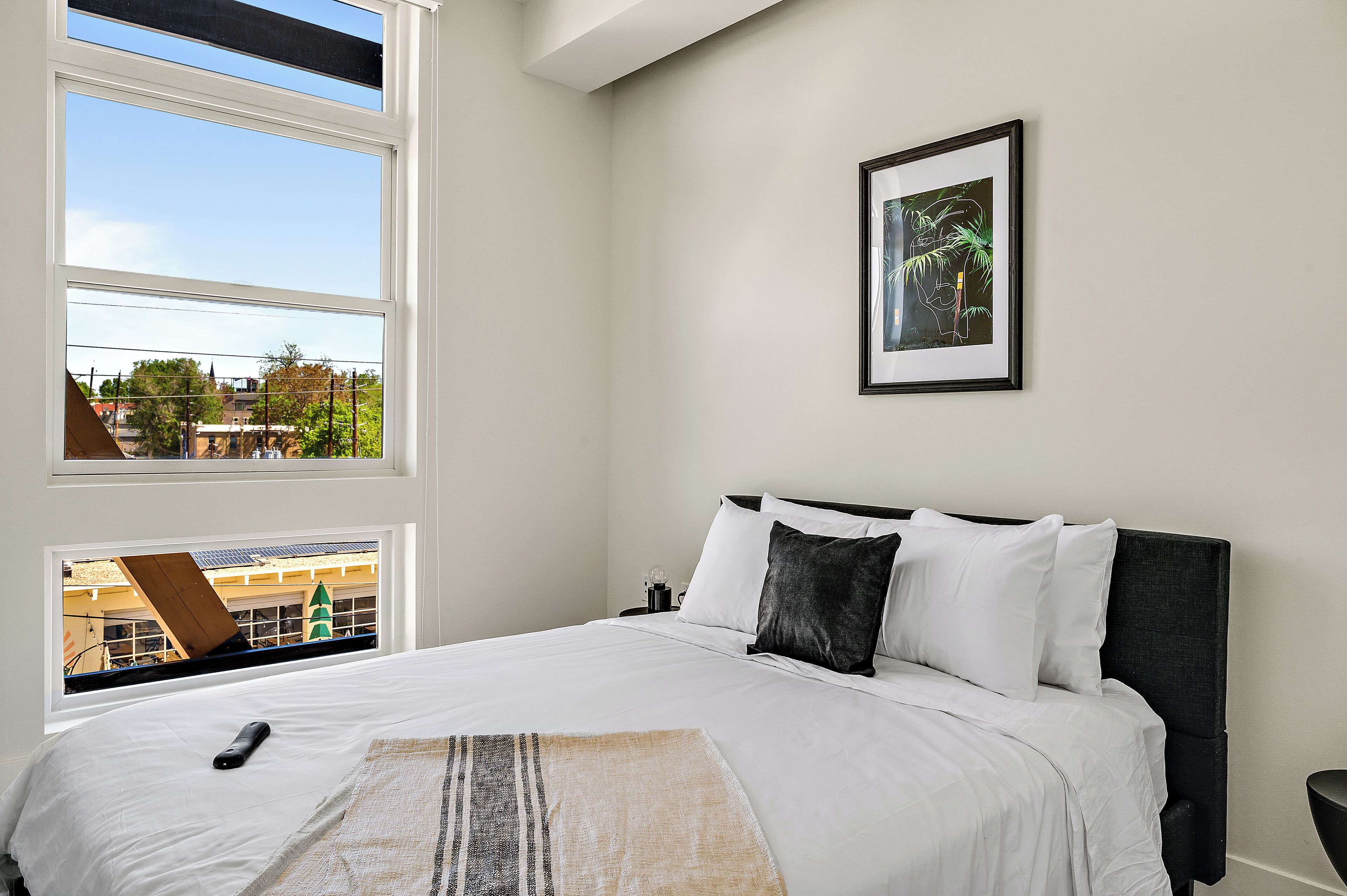 A neatly made bed with white linens, a black headboard, and a framed picture on the wall.