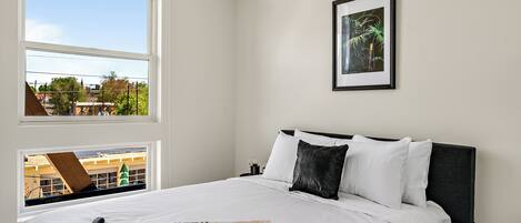 A neatly made bed with white linens, a black headboard, and a framed picture on the wall.