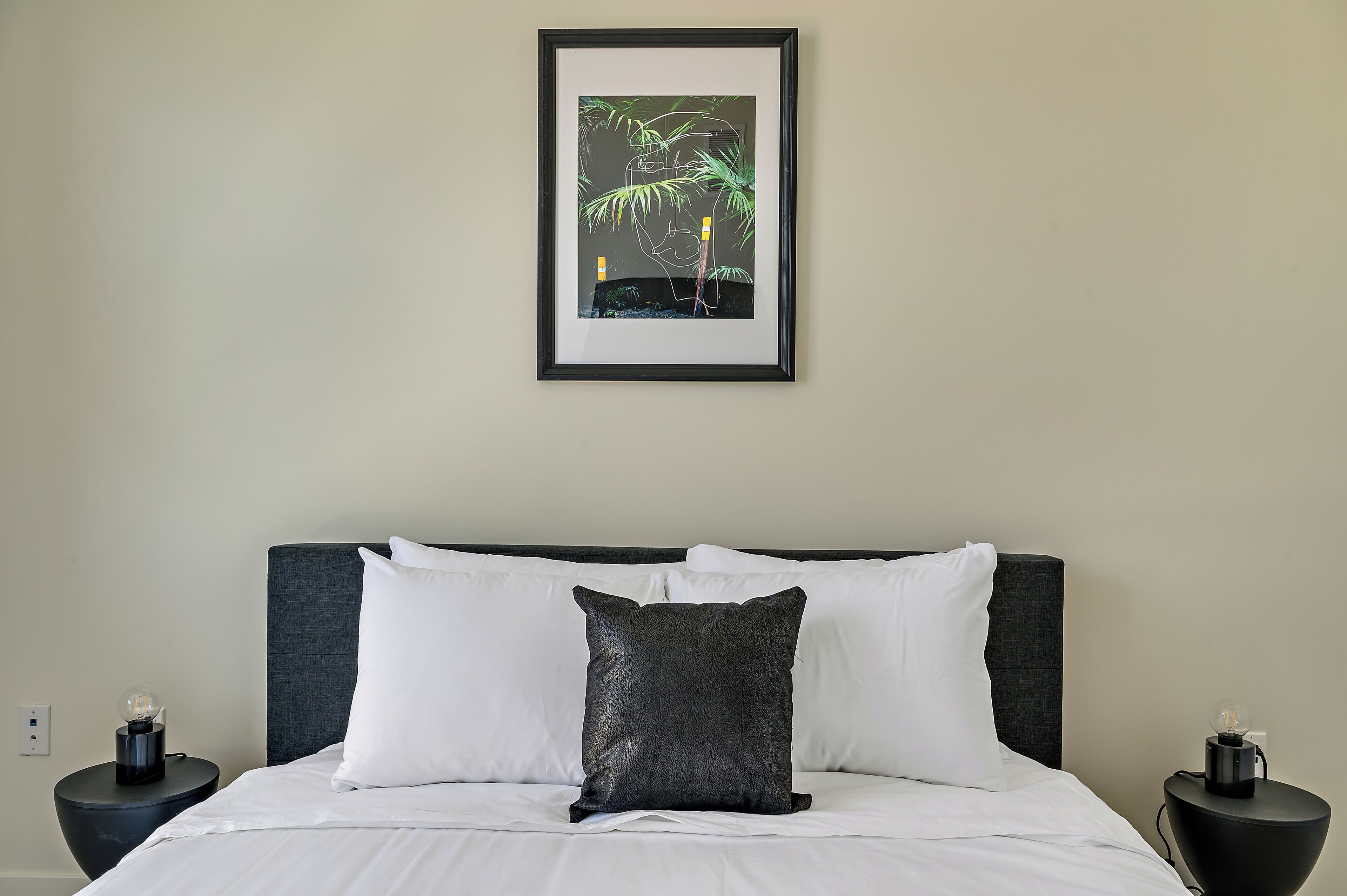 A neatly made bed with white linens and a dark gray pillow, flanked by two black nightstands with lamps.