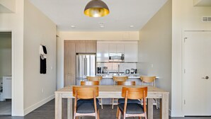 Una cocina moderna con armarios blancos, electrodomésticos de acero inoxidable y un comedor con sillas y mesa de madera.