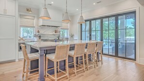 A modern kitchen with a large island, pendant lighting, and a view to the outdoors. - 2410 The Bent Twig (Seabrook Island)