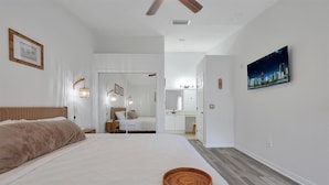 A bedroom with a large bed, a bedside lamp, a mirror, a painting on the wall, and a view into the bathroom. - 2722 Club Cortile Unit B 3bed (Kissimmee)