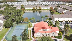 A residential area with a large body of water, tennis courts, and a prominent building with a red roof. - 2722 Club Cortile Unit B 3bed (Kissimmee)