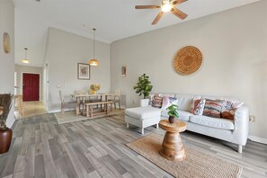 A spacious living room with a dining area, a ceiling fan, and a large woven wall hanging. - 2722 Club Cortile Unit B 3bed (Kissimmee)