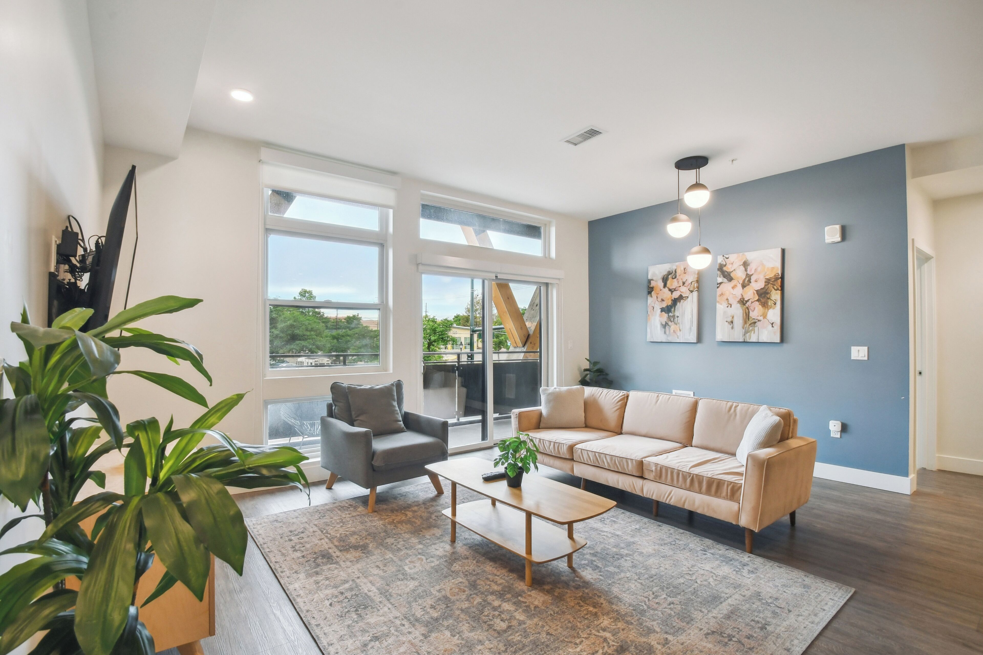 Een moderne woonkamer met een bank, fauteuil en salontafel, grote ramen en kunst aan de muur.