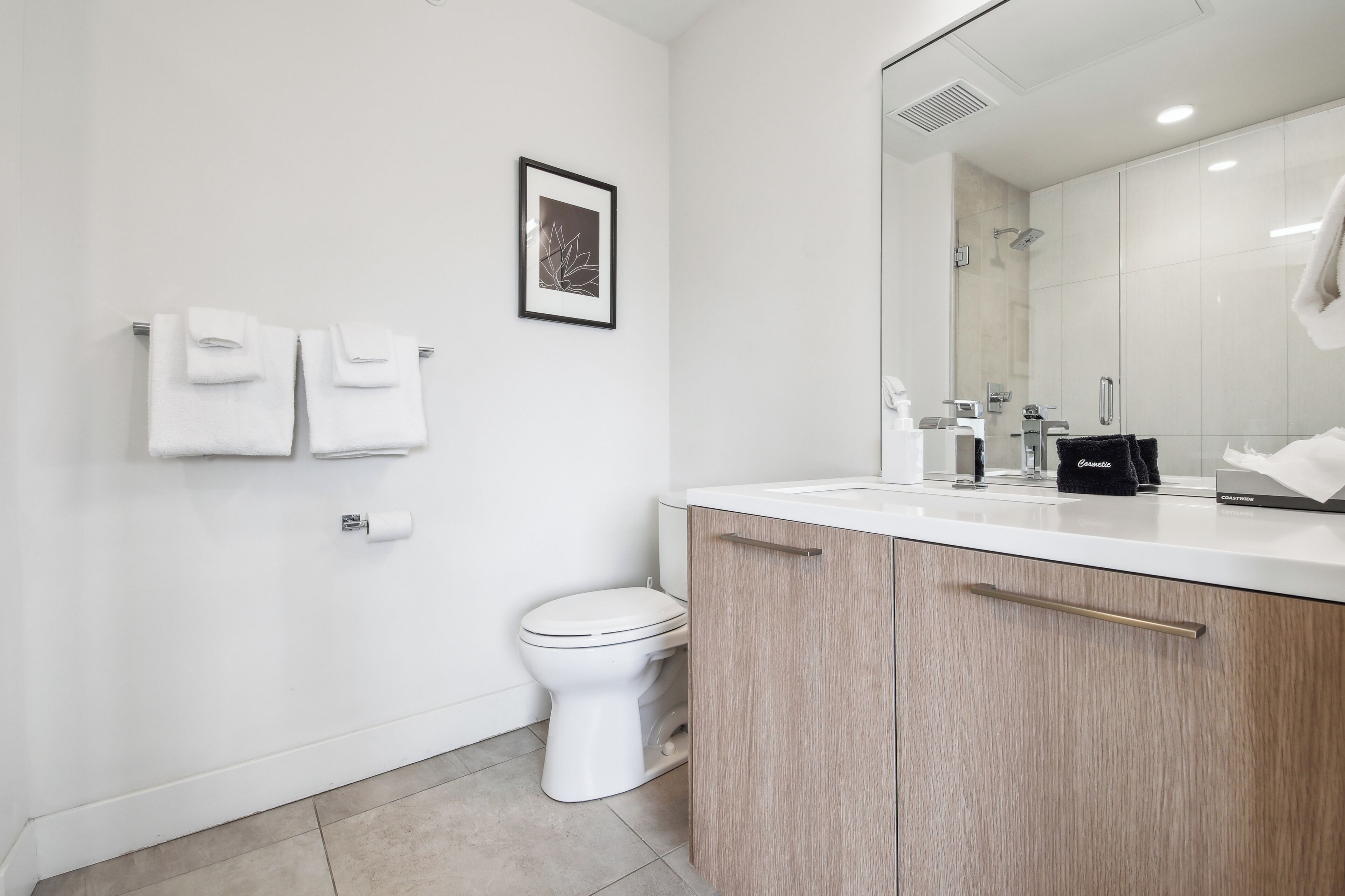 Ein modernes Badezimmer mit einer weißen Toilette, einem Waschbecken mit Spiegel und Holzschränken.