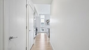 Un pasillo estrecho con paredes blancas y suelo de madera, que conduce a una zona de cocina con electrodomésticos modernos.