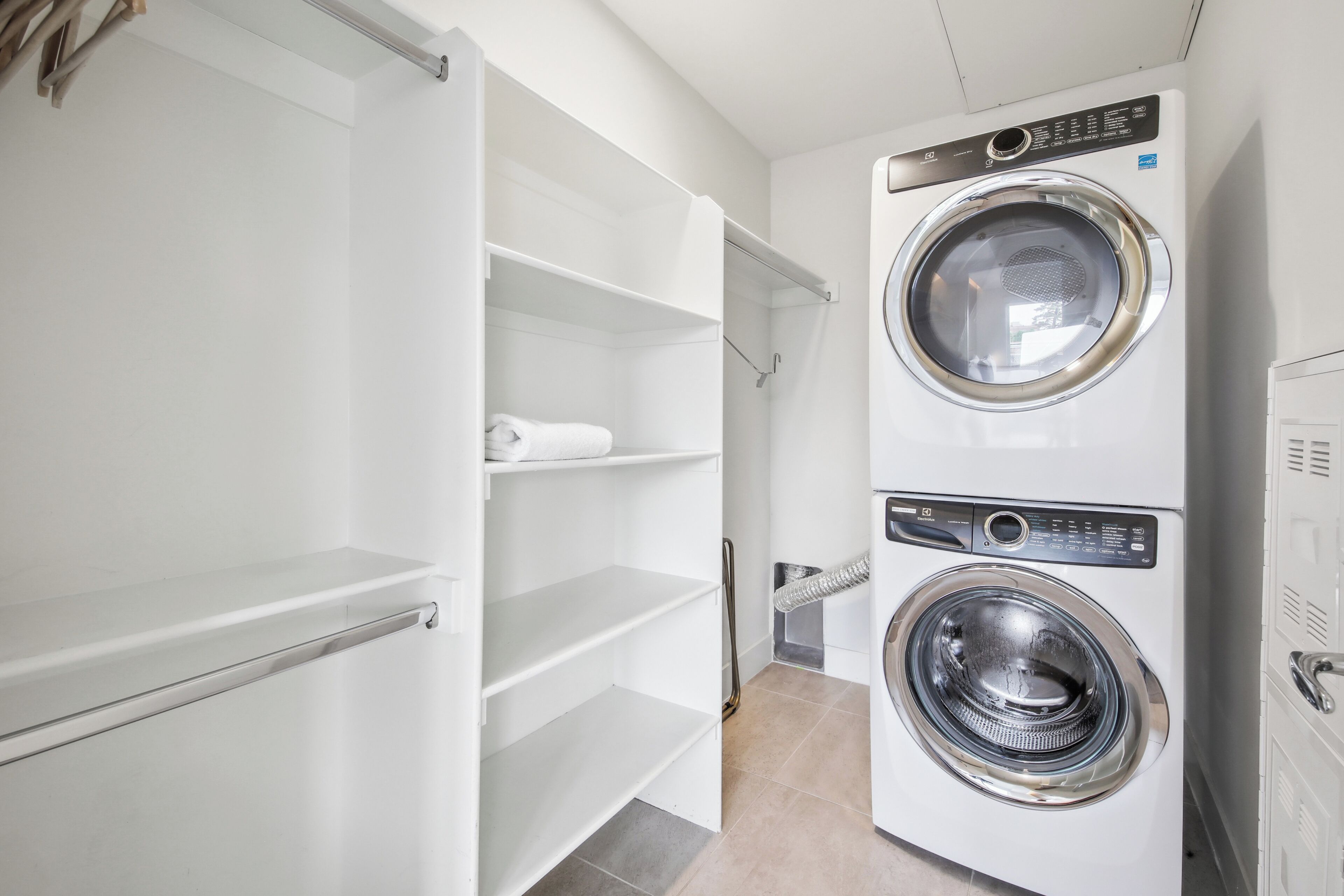 A laundry room with a front-loading washer and dryer, open shelving, and a towel rack.