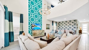 A modern living room with a large beige sectional sofa, a flat-screen TV, and a geometric patterned accent wall. - 2758bd · Dazzling 5BR Villa in Storey Lake With Pool & Spa (Kissimmee)