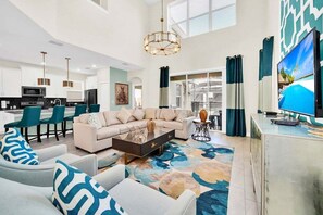 A spacious living area with a sofa, coffee table, and chairs, a kitchen with modern appliances, and a large TV screen. - 2758bd · Dazzling 5BR Villa in Storey Lake With Pool & Spa (Kissimmee)