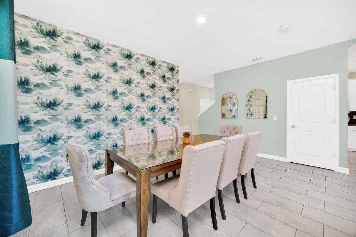 Un coin repas avec une table à plateau en verre et six chaises rembourrées, un mur à motifs et une porte blanche en arrière-plan.