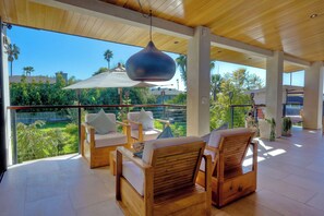 Un balcon spacieux, agrémenté de meubles en bois, d’un luminaire suspendu et offrant une vue sur la verdure et les bâtiments.