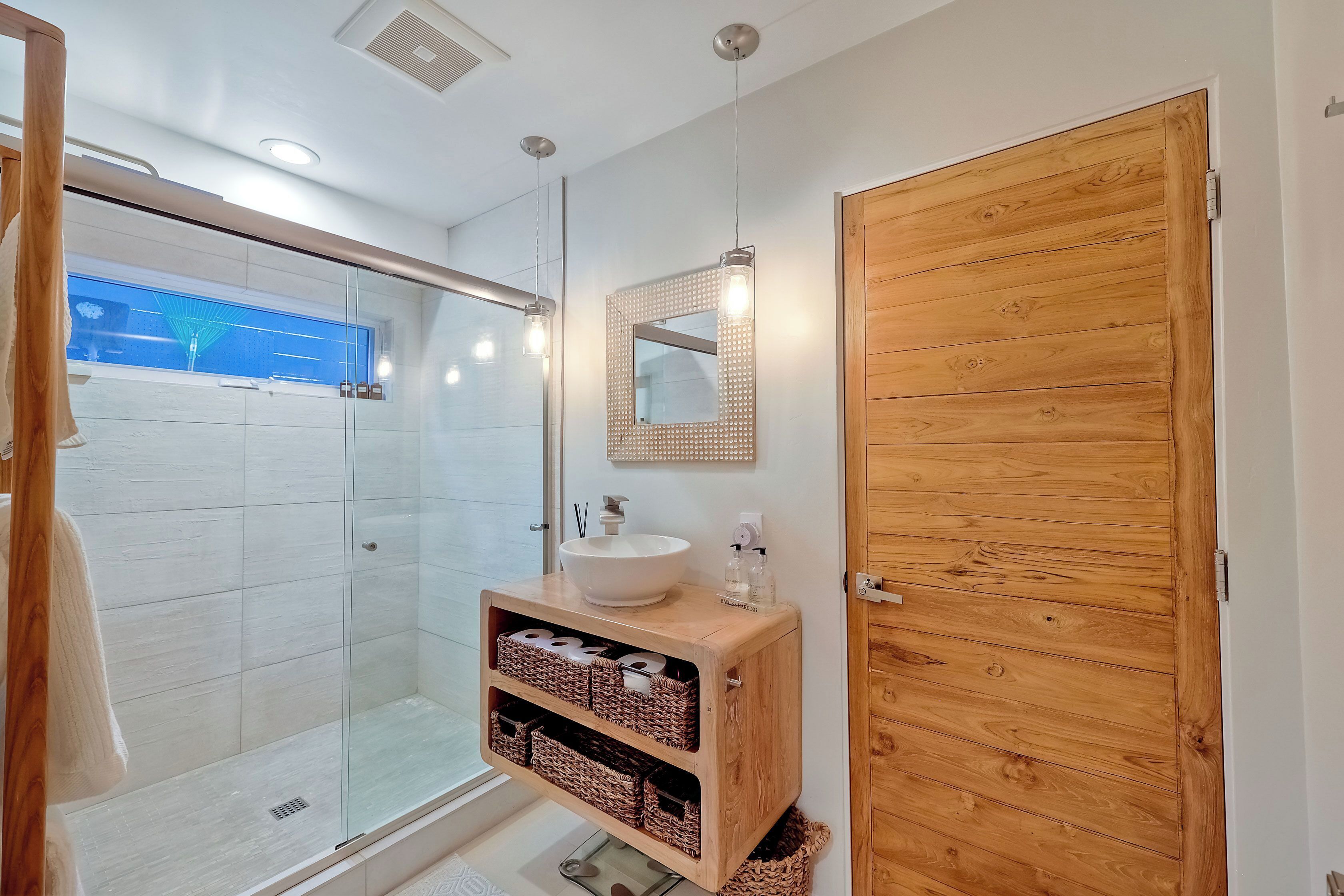 A modern bathroom with a glass shower enclosure, a wooden vanity with a white sink, and a wooden door.