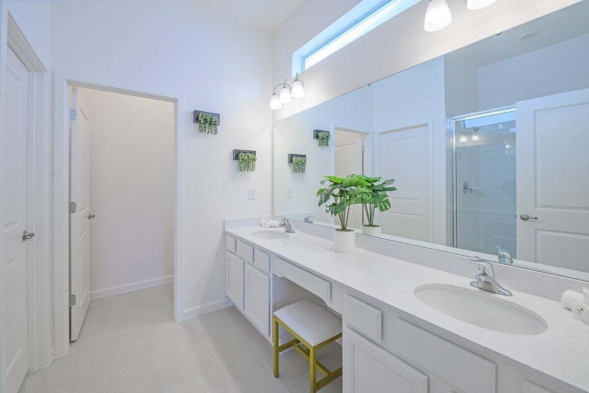 A modern bathroom with two sinks, a large mirror, and a potted plant.