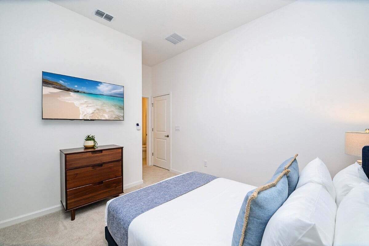 Een slaapkamer met een bed, een kaptafel, een schilderij van een strand en een deur die naar een andere kamer leidt.