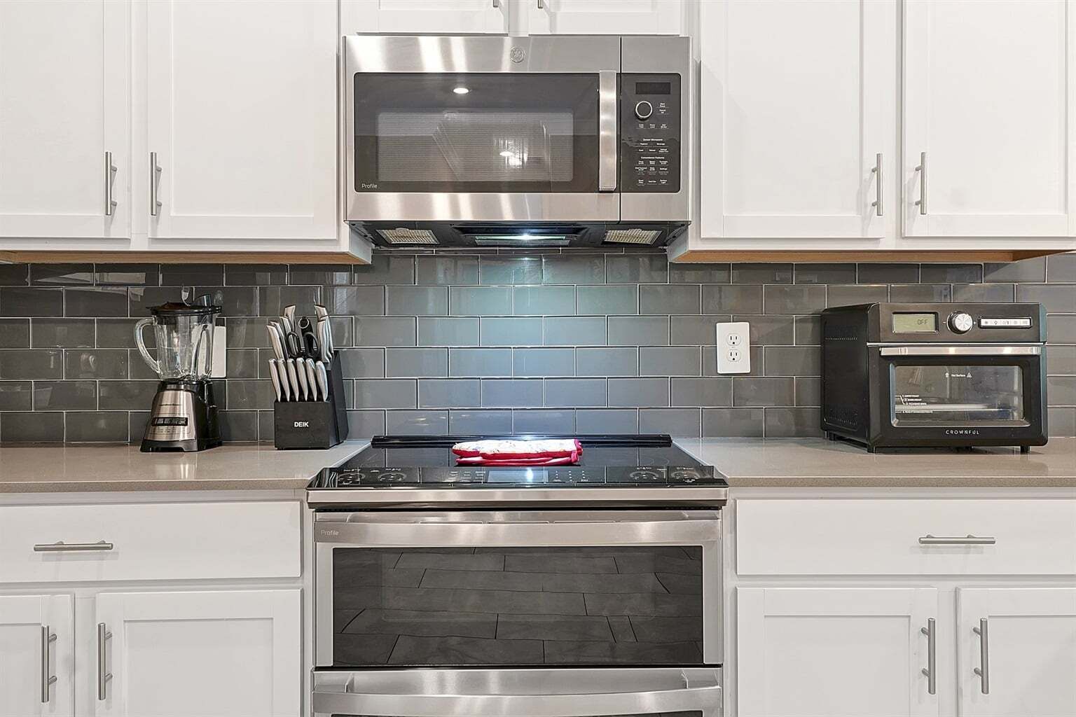 A kitchen with white cabinets, a stainless steel microwave, a built-in oven, a toaster, and a blender on the counter.