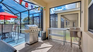 An outdoor patio with a grill, a sink, and a dining area with chairs and a table. - 2473 Shanti · Deepsea World/15 Suites/sleep 30/oversize Pool&spa (Kissimmee)