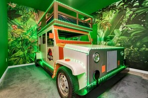 A double-decker bus-themed room with green ambient lighting and a jungle mural. - 2473 Shanti · Deepsea World/15 Suites/sleep 30/oversize Pool&spa (Kissimmee)