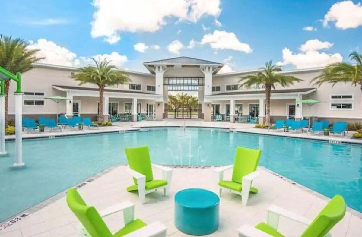 A pool area with a central pool, surrounded by lounge chairs and palm trees.