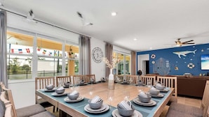A dining area with a long table set for a meal, surrounded by chairs. - 2473 Shanti · Deepsea World/15 Suites/sleep 30/oversize Pool&spa (Kissimmee)