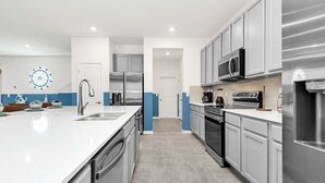 A modern kitchen with stainless steel appliances, a large island, and blue accent walls. - 2473 Shanti · Deepsea World/15 Suites/sleep 30/oversize Pool&spa (Kissimmee)