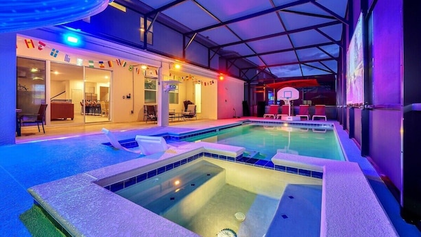 An indoor swimming pool with a glass ceiling, lounge chairs, and a basketball hoop. - 2473 Shanti · Deepsea World/15 Suites/sleep 30/oversize Pool&spa (Kissimmee)