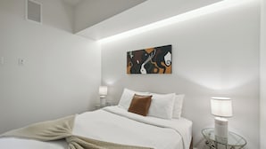 Een moderne hotelkamer met een opgemaakt bed, een abstract schilderij aan de muur en een nachtkastje met een lamp.