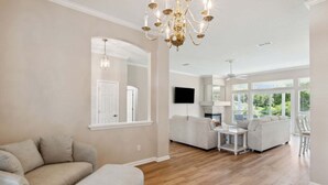 A spacious living room with a large chandelier, a fireplace, and a view of greenery outside. - 2888 Tidewater Drive (Fernandina Beach)
