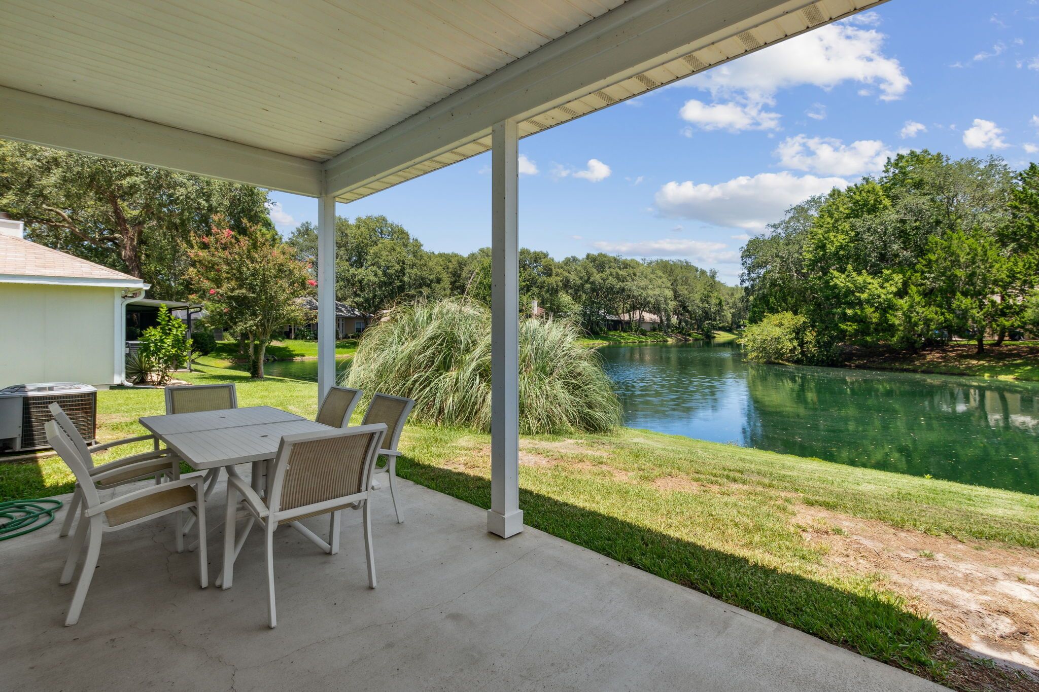 A covered patio with a table and chairs, overlooking a lake and lush greenery.