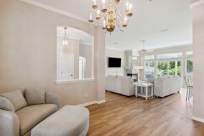 A spacious living room with a large sofa, a coffee table, and a chandelier. - 2888 Tidewater Drive (Fernandina Beach)