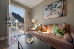 A living room with a brown leather sofa, tropical-themed pillows, a black coffee table with a decorative leaf, and a beach-themed painting on the wall. - 2501 W North B St, Unit 8 (Tampa)