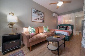 A cozy room with a sofa, a small table, a bed, and a wall-mounted lamp. - 2501 W North B St, Unit 8 (Tampa)