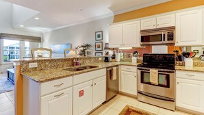Una cucina moderna con mobili bianchi, piani in granito, elettrodomestici in acciaio inossidabile e un'ampia finestra che lascia entrare molta luce naturale.
