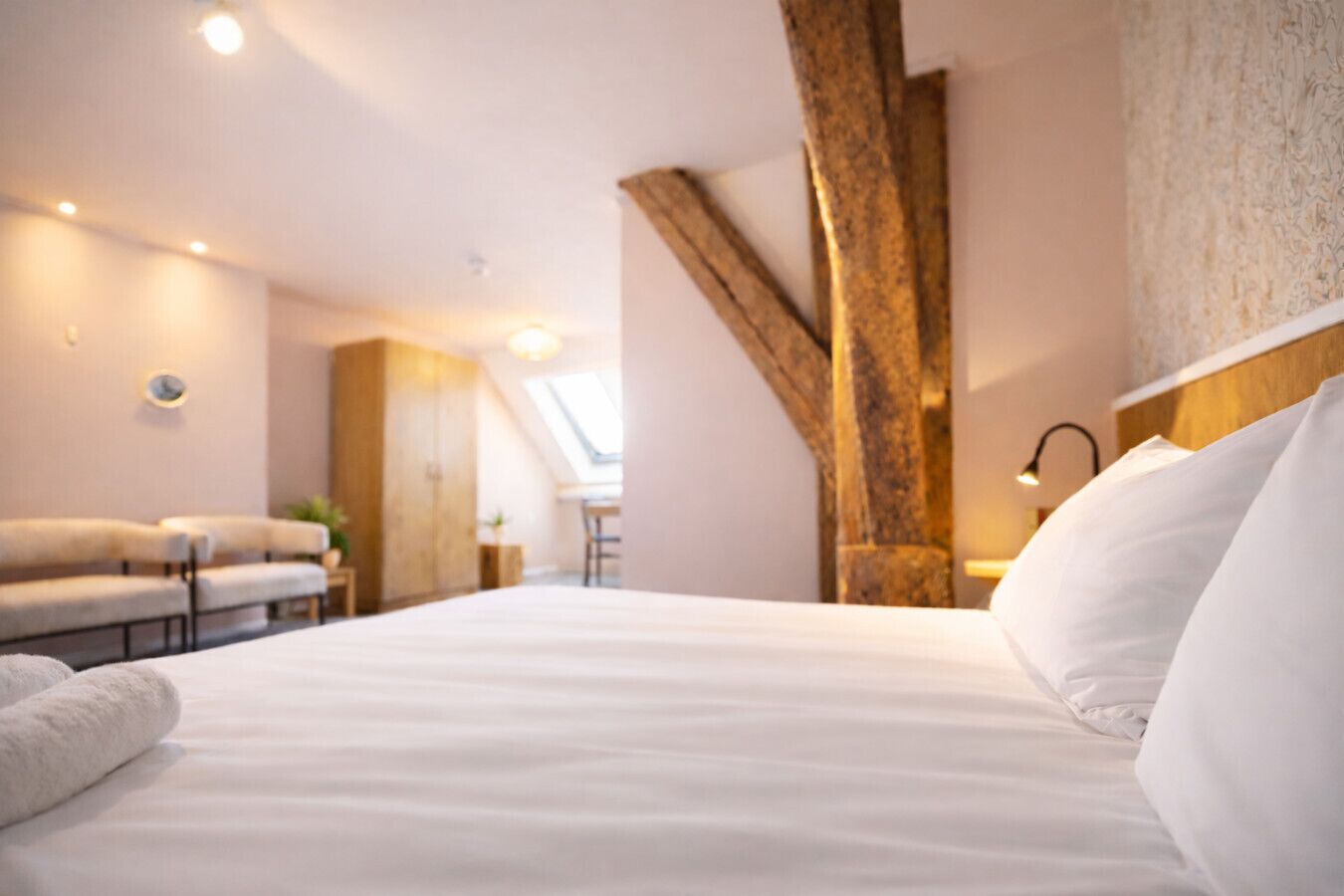 A modern hotel room with a large bed, a wooden accent wall, a small table with a lamp, and a view of the outdoors.
