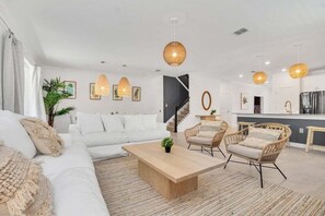 A modern living room with a white sofa, two wicker chairs, a wooden coffee table, and a staircase leading to an upper level. - 2706ow · Brand New Storey Lake 10 Bedroom Villa With Pool & (Kissimmee)