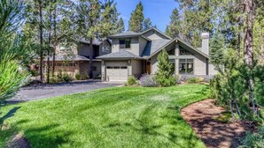 A two-story house with a garage, surrounded by a well-maintained lawn and tall pine trees. - 28 Big Leaf (Bend)