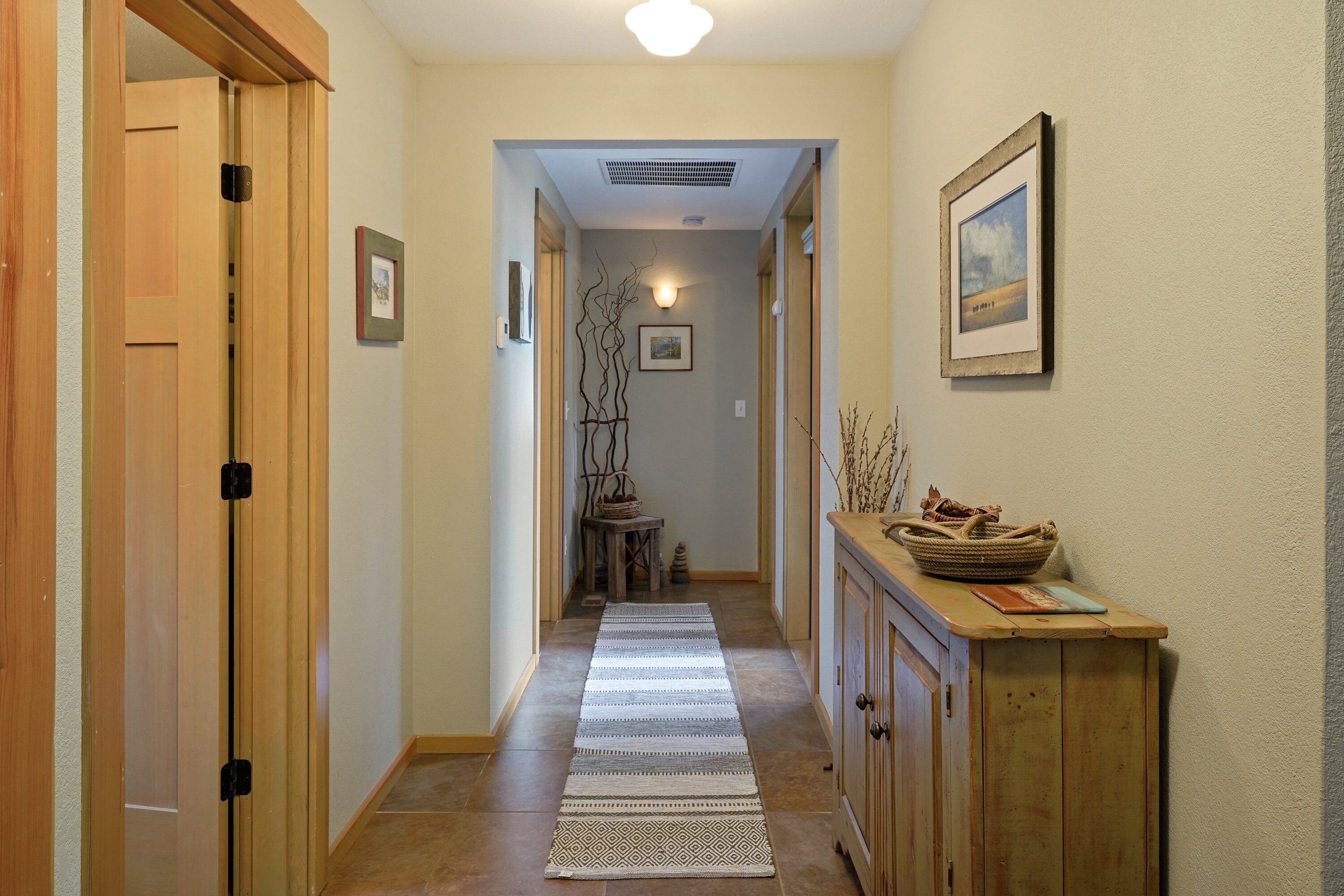 Un couloir avec une porte en bois, un tapis, une armoire et un tableau encadré au mur.