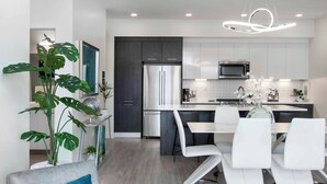 A modern kitchen with white cabinets, stainless steel appliances, and a dining area with white chairs and a glass table. - 2880: Above the Cityline Elegance at Espadin (Denver)