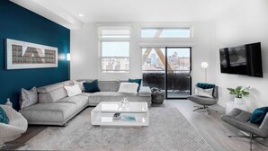 A modern living room with a grey sectional sofa, a white coffee table, and a grey armchair. There is a large window with a view of buildings and a balcony. - 2880: Above the Cityline Elegance at Espadin (Denver)