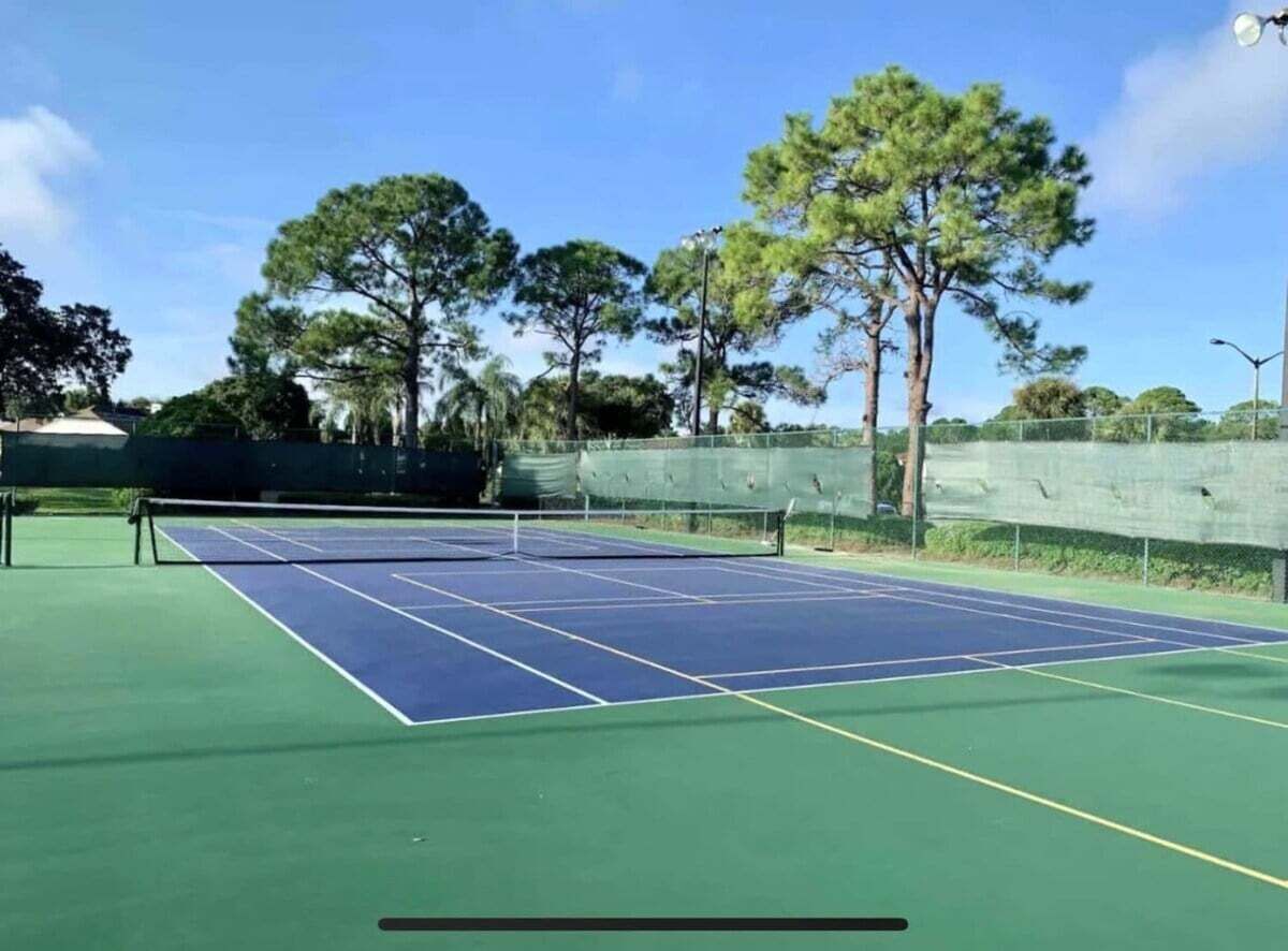 A tennis court with a net, surrounded by trees and a fence.